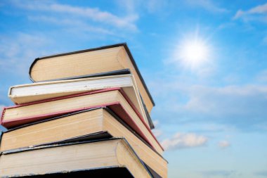 Stack Of Books Against Blue Sky. The sky is full of clouds floating around, both small and large, the sun is shining brightly
