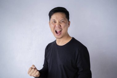 Mutlu galip. Çimento duvarının önünde dikilirken el kol hareketi yapan ve ağzını açık tutan mutlu genç adam..