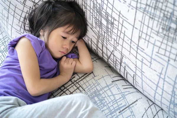 Distracted sad Asian girl looks out on the sofa in the living room at home. think of grief feel desperate sit alone