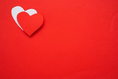 Kırmızı arka planda izole edilmiş kırmızı kağıt kalpler. Sol üstte metin eklemek için boş bir boşluk var.