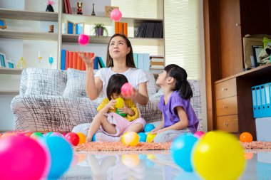 Bir anne, iki Asyalı kız, evde mutlu mesut oynuyorlar, anne ve kız gülümsüyor, rüzgar topuyla birlikteler. Annem havaya üç top atıyordu..