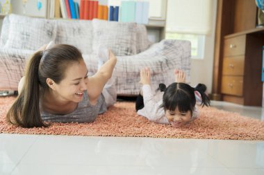 Güzel genç kadın ve sevimli kızı evde yoga yaparken gülümsüyorlar.