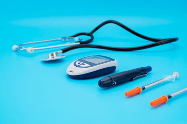 Kandaki glikoz seviyesini ölçmek için aygıt, test şeridi ve mavi arka planda steteskop.