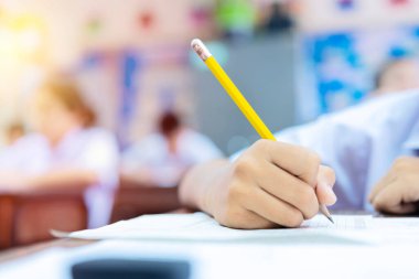 Okul öğrencileri çok çalışıyor, kafaları el üstünde oturuyor, beyaz kağıtlara notlar okuyor ve not alıyor, sınav konseptine giriyorlar.