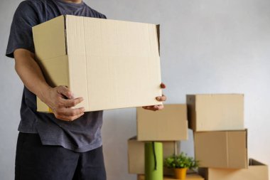Yeni evde açık karton kutu taşıyan bir adamın orta kısmı, eve taşınırken elinde karton kutular tutan bir adamın kırpılmış görüntüsü.