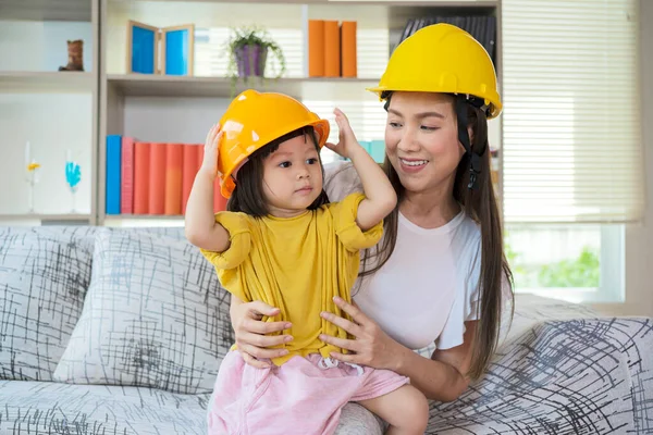 An Asian mother and daughter play as an engineer in command, with yellow helmet-playing equipment.