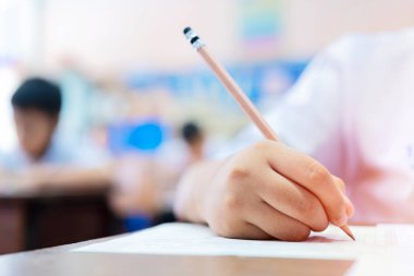 Okul öğrencileri çok çalışıyor, kafaları el üstünde oturuyor, beyaz kağıtlara notlar okuyor ve not alıyor, sınav konseptine giriyorlar.