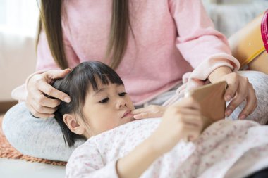Güzel bir anne ve küçük bir kız evde halıda otururken akıllı telefonlar kullanıyor ve gülümsüyorlar..