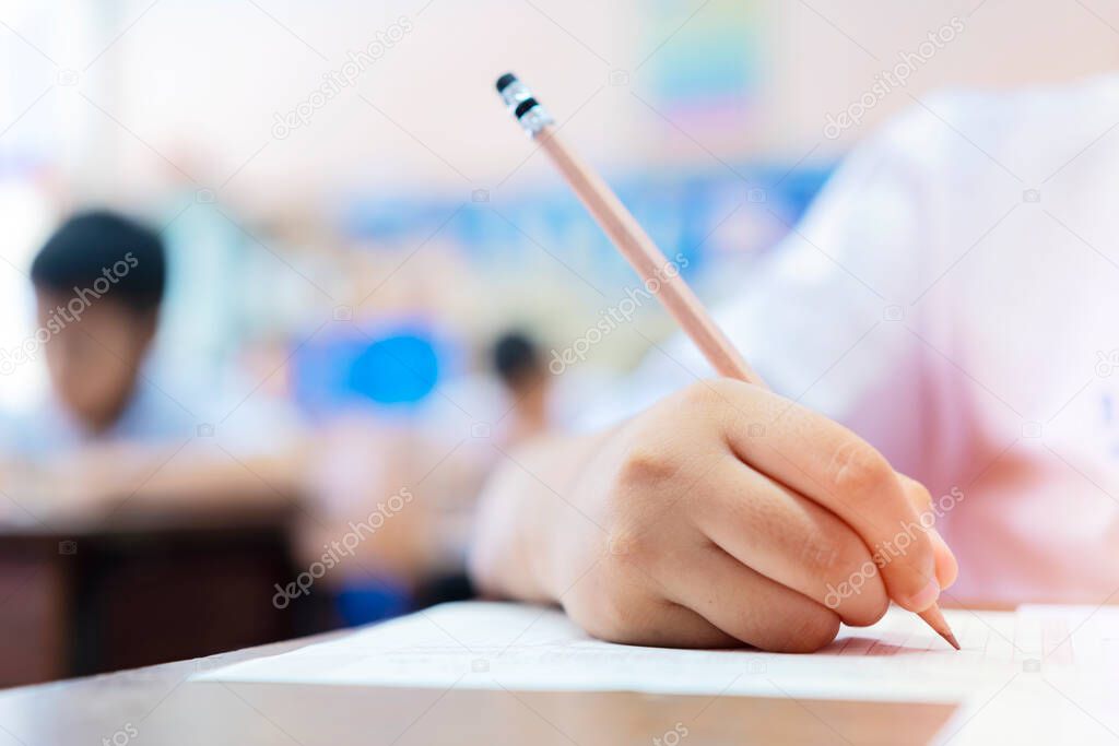 School students hard at work in the classroom sitting with his head on his hand reading and writing notes on sheets of white paper, taking exam concept