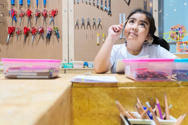 Masalarında el sanatları yapan mutlu çocuklar icat edeceği şeyi düşünüyordu..