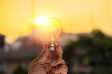 Gün batımı enerjili bir ampulü tutan el, sürdürülebilir gelişim. Ekoloji kavramı