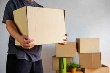 Yeni evde açık karton kutu taşıyan bir adamın orta kısmı, eve taşınırken elinde karton kutular tutan bir adamın kırpılmış görüntüsü.