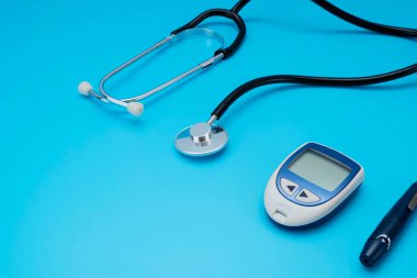 Kandaki glikoz seviyesini ölçmek için aygıt, test şeridi ve mavi arka planda steteskop.
