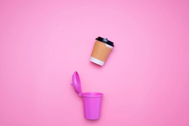 Kağıt kahve fincanları pembe arka plandaki pembe çöpe düşmek üzere..