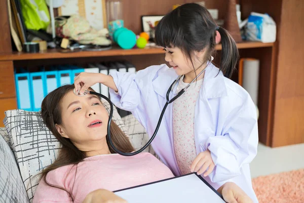Cute little Asian girl act as nurse hold stethoscope listen to mom heart playing together at home, small Vietnamese child as doctor take care of mother or nanny, engaged in funny activity in bedroom