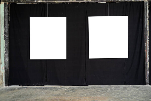 Two white picture frames were hung in a gallery on a black fabric wall.