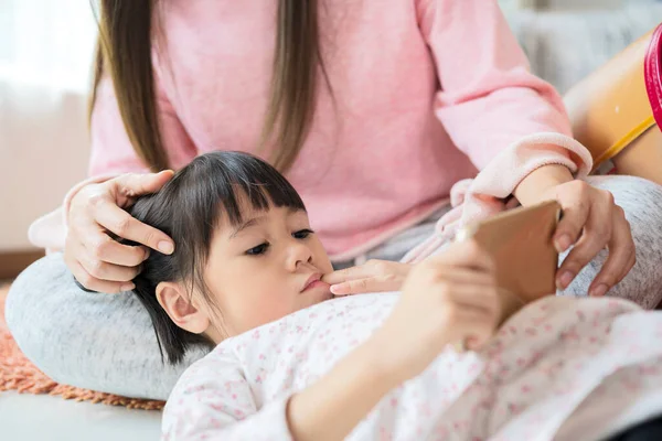 Güzel bir anne ve küçük bir kız evde halıda otururken akıllı telefonlar kullanıyor ve gülümsüyorlar..