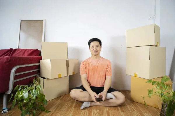 幸せな男は新しい家に喜んで休憩座って移動します 壁の背景に段ボール箱を持つ若い男 — ストック写真