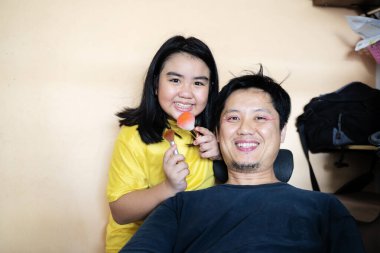 Şirin kız babasına makyaj yapıyor, yatak odasında yatakta oturuyor. Aile tatili ve birliktelik. Komik zaman, baba ve çocuğu evde oynuyorlar.. 