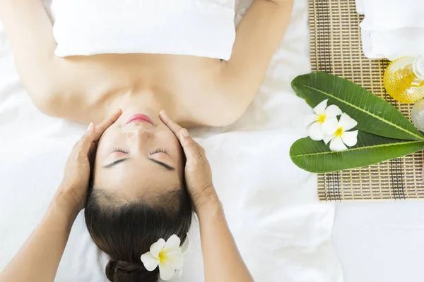 portrait of young beautiful woman in spa environment, wellness, beauty and relaxation concept - beautiful young woman lying with closed eyes and having face and head massage at spa