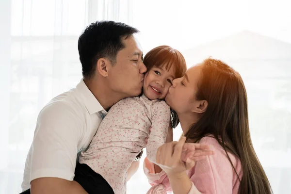 Portrait of attractive asian dad and mom kissing daughter\'s cheek together close up on isolated white studio background. Parenthood and childhood lifestyle or love and bonding in soft tone concept.