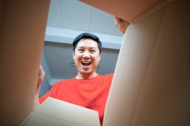 Gülümseyen adam bir karton kutuyu açıp içine bakıyor, yer değiştiriyor ve paketleri açıyor.