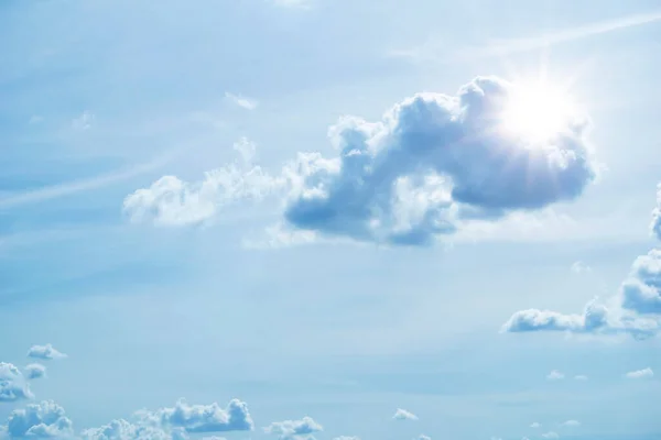 Sun in blue sky with cloud. View of the blue sky with white cumulus clouds and the bright sun with rays and highlights