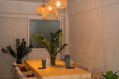 Konforlu modern yemek odası iç tasarımı ahşap bir masa, yeşil iç mekan bitkileri ve sıcak kolye ışıkları dekorasyon, yaşam tarzı, mobilya kavramları için ideal, rahatlatıcı bir ev atmosferi yaratıyor..