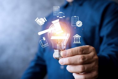 Hukuku, adaleti, politikayı ve yeniliği temsil eden yasal simgelerle parlayan bir ampulü elinde tutan bir iş adamı. Hukuki teknoloji kavramı, fikri mülkiyet ve modern iş için düzenlemeler.