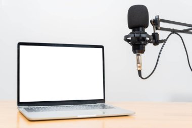 Modern laptop with blank white screen beside a studio microphone on adjustable arm, creating a clean podcast workspace scene ideal for themes of content creation, streaming, broadcasting.