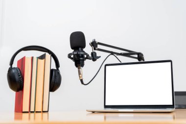 Modern laptop with blank white screen beside a studio microphone on adjustable arm, creating a clean podcast workspace scene ideal for themes of content creation, streaming, broadcasting.