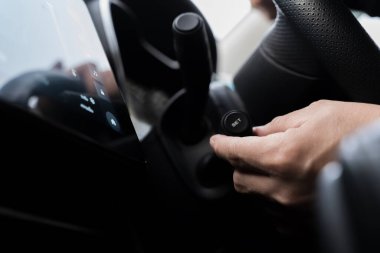 Bir sürücünün modern bir arabanın içinde hız kontrol düğmesini ayarlarken yakın plan çekimi, güvenlik, kolaylık ve sürüş odaklarını vurguluyor. El, düğme ve iç aydınlatma teknolojisinin ayrıntıları.