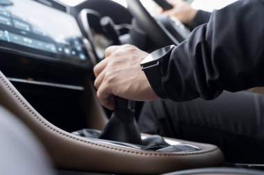 Modern bir arabanın içinde vitesi değiştiren bir sürücünün yakın çekim görüntüsü, kontrol, hareket ve sürüş odaklarını vurguluyor. Resim el hareketlerini, iç ayrıntıları ve ulaşım kavramlarını yakalar.