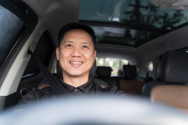 Emniyet kemeriyle araba süren neşeli bir adamın portresi, modern bir aracın içinde güvenle gülümseyen, güvenli sürüş gösteren, pozitif duygu, ve ön camdan dışarı doğru gülen.