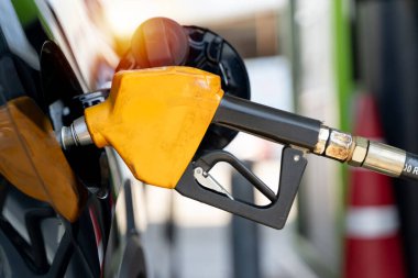 Benzin deposunu dolduran sarı bir benzin pompasının yakın çekimi. Ulaşım, enerji tüketimi, benzin fiyatı ve yakıt ikmali kavramı.