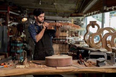 Profesyonel Luthier, işlek bir atölyede el yapımı üretim, hassasiyet ve enstrüman yapımını gösteren aletler ve gitar kalıpları ile boş bir tahta gitar boyun hizasını kontrol eder..