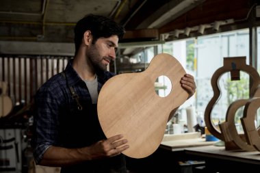 Önlüklü Luthier bitmemiş bir akustik gitarı bir marangozhanede inceledi. Özel enstrüman yapımı, ahşap işçiliği, kalite kontrolü ve zanaatkar üretim kavramı.