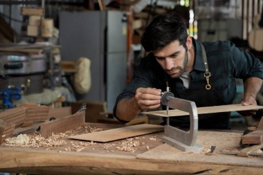 Odaklanmış marangoz, işlek bir marangoz atölyesinde aletler ve ahşap talaşlarıyla düzgün şekiller ve şablonlar yaratmak için bir parşömen testeresi kullanır..