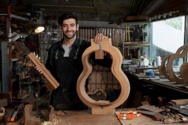 Bir ahşap atölyesinde gitar küf ve boyun boşluğu tutan önlüklü bir gitarcının portresi. El yapımı enstrüman, zanaatkarlık, araçlar ve şablonlar.