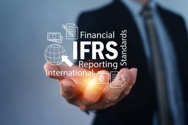 IFRS metnini küresel finans simgeleri ve parlayan ellerle sunan bir işadamı. Uluslararası muhasebe standartları, mali raporlama, uyum, denetleme, kurumsal yönetim ve yönetmelik kavramı.