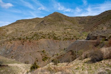 Mavi ve bulutlu gökyüzünün altında taşlı ve gür dağlar