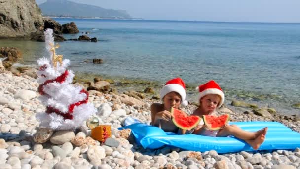 Niños en sombrero de Navidad están comiendo sandía en la playa — Vídeos de Stock