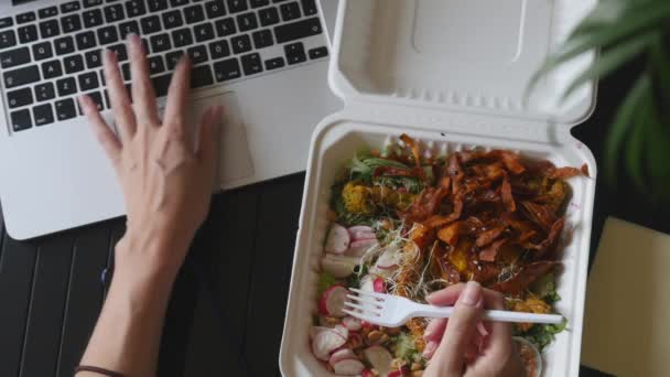 Vue du dessus de la femme travaillant sur ordinateur portable et manger de la nourriture dans la boîte — Video