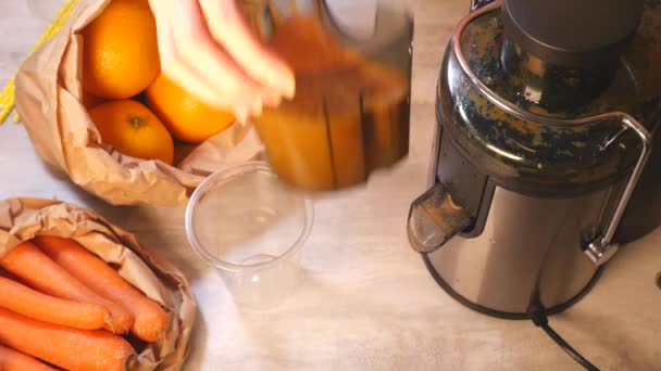 Γυναικεία χέρια ρίχνει φρέσκο καρότο και χυμό πορτοκαλιού σε πλαστικό κύπελλο — Αρχείο Βίντεο