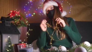 Maskeli genç bir kadın ve Noel Baba şapkası evde eğleniyor.