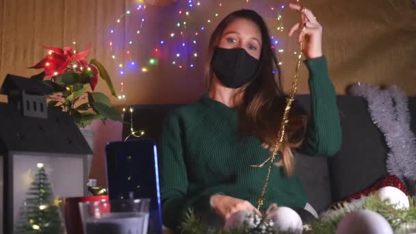 Молодая женщина в маске делает видеозвонок и весело проводит время дома — стоковое видео