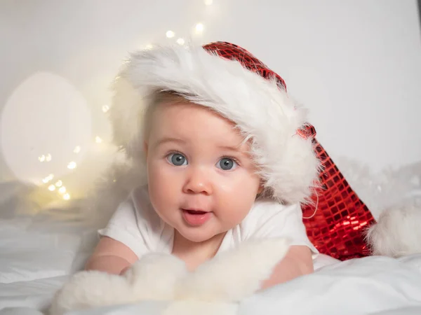 Adorable petite fille dans le chapeau de Père Noël couché sur le lit et souriant — Photo