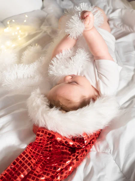 Adorable petite fille dans le chapeau de Père Noël couché sur le lit et jouer — Photo