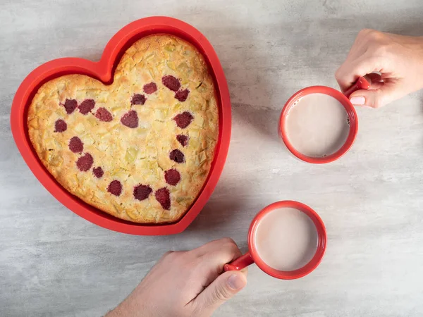 Heart shape cake silicon mould with hot drink cups in couple hands — Stock Photo, Image