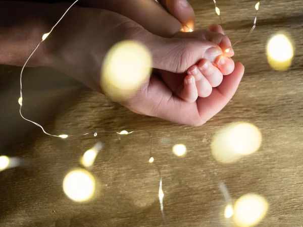 Κλείσιμο του πατέρα κρατώντας το χέρι του μωρού με τα χριστουγεννιάτικα φώτα — Φωτογραφία Αρχείου